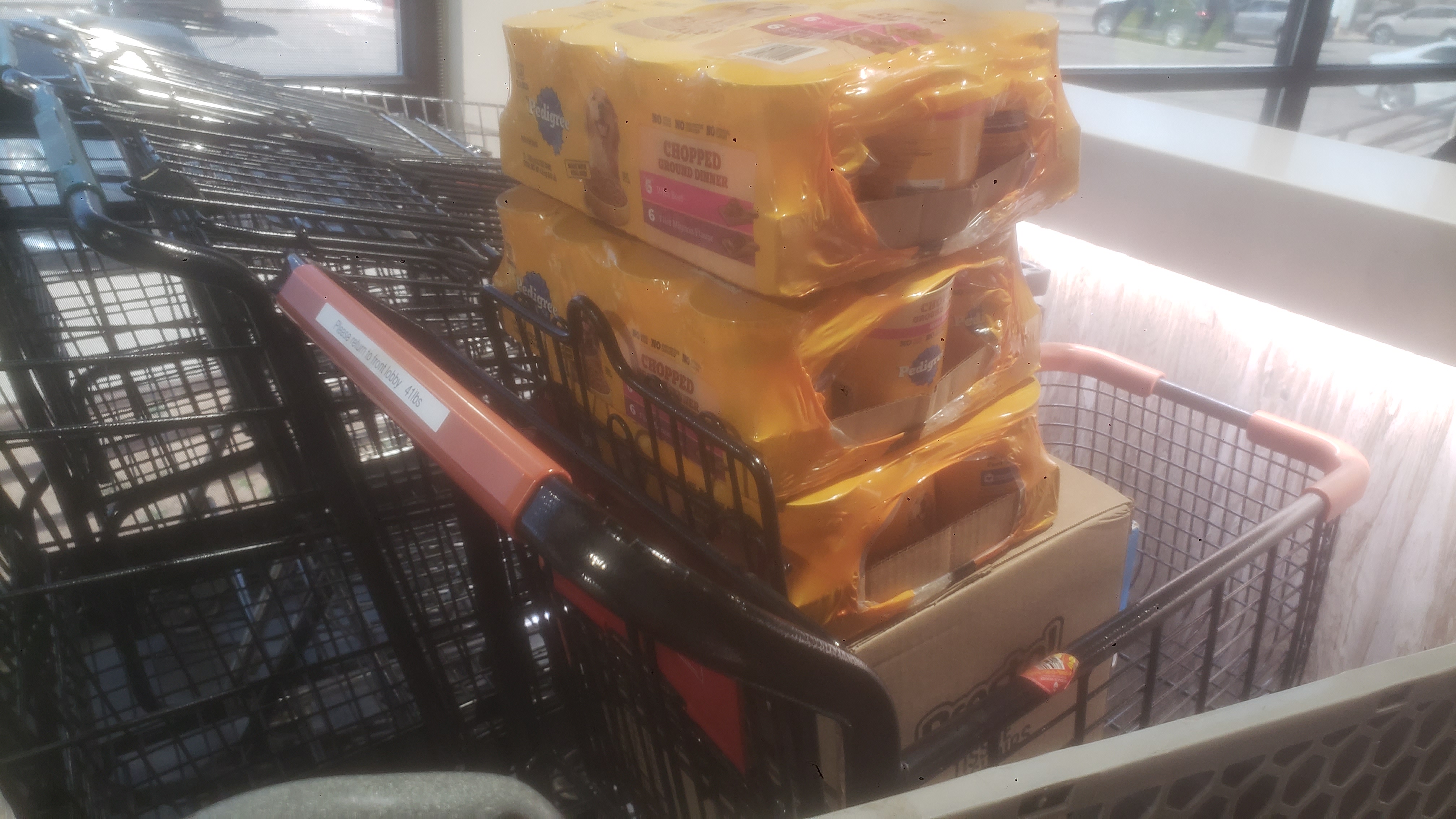 Cans of dog food on top of box in a shopping cart.
